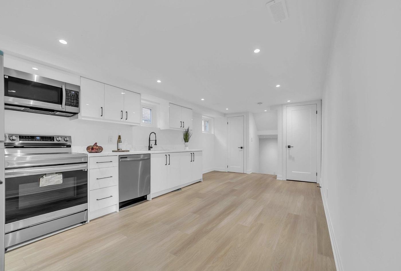 Finished basement with a white kitchenette, pot lights and light oak vinyl plank flooring in Woodbridge, by NewGen Renovations Vaughan