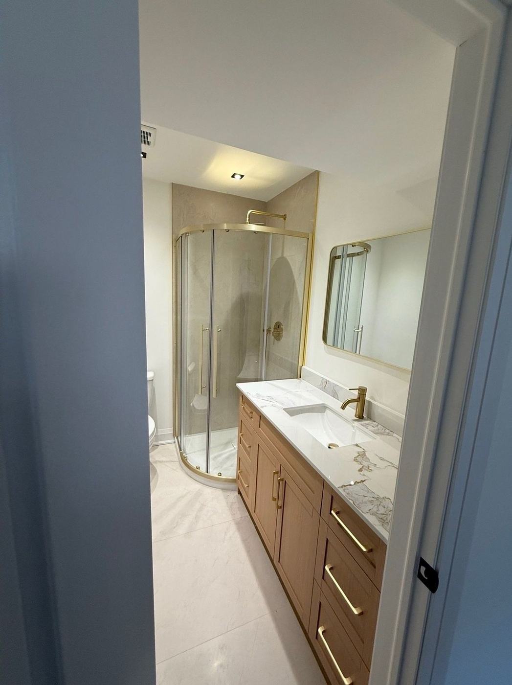 Bathroom with a round glass shower, brushed gold fixtures and a floating oak vanity in Concord, by NewGen Renovations Vaughan
