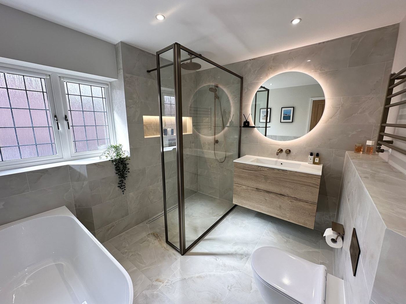 Bathroom renovation with a bronze-framed walk-in shower, backlit round mirror and floating oak vanity in Richmond Hill, by NewGen Renovations Vaughan