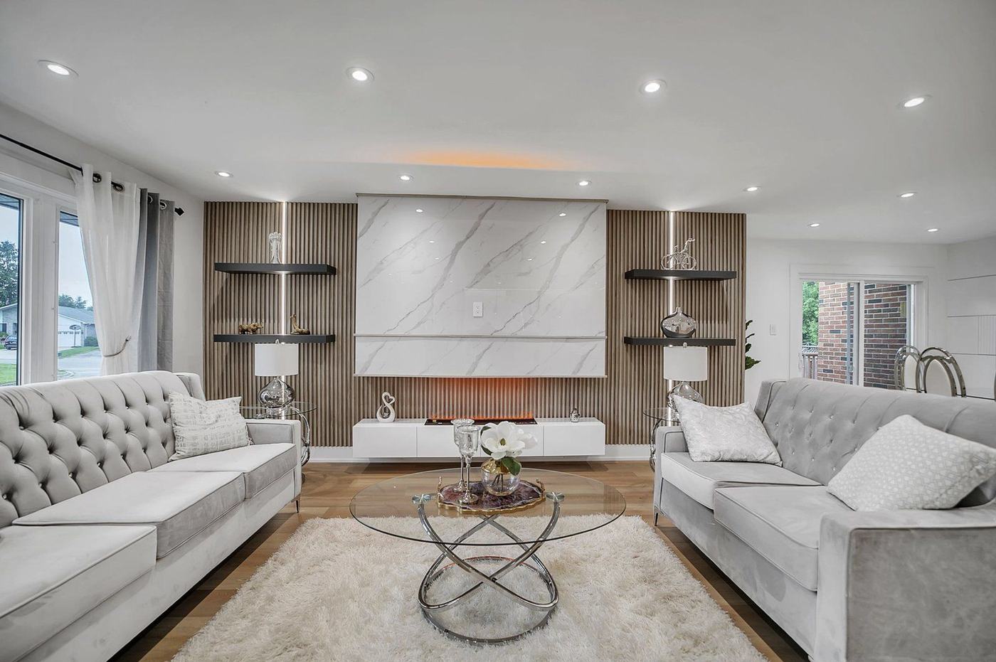Renovated living room with a slatted wood and marble-look feature wall, built-in electric fireplace, floating shelves, pot lights and new flooring, by NewGen Renovations Vaughan