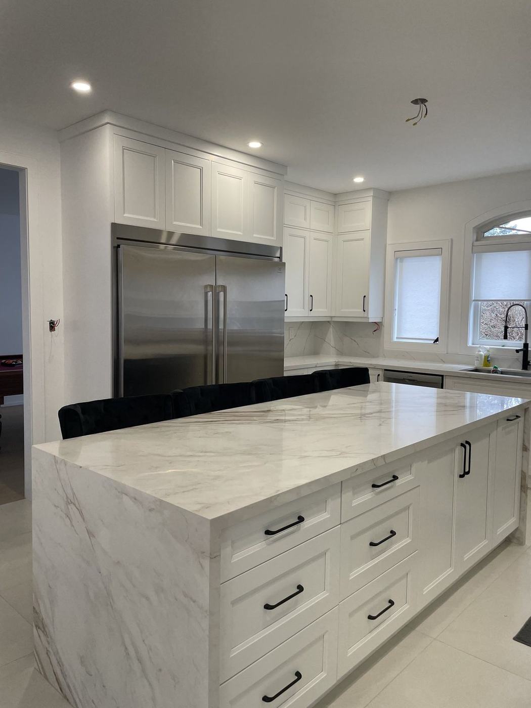 White shaker kitchen with a marble-look waterfall island, black hardware and a built-in stainless fridge, renovated by NewGen Renovations Vaughan